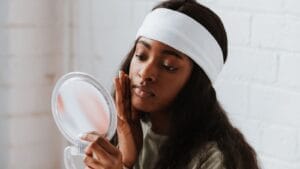 Black woman applying moisturiser while checking dry skin in a mirror