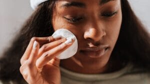 Black woman gently cleansing her face while checking her skin in a mirror